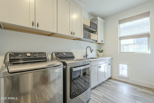 clothes washing area with light hardwood / wood-style floors, cabinets, separate washer and dryer, and sink