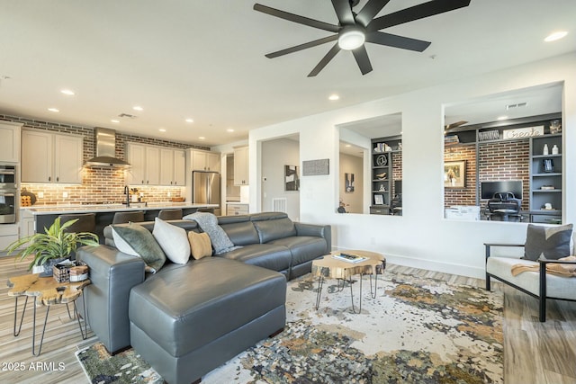 living room with light wood-type flooring, built in features, ceiling fan, and sink