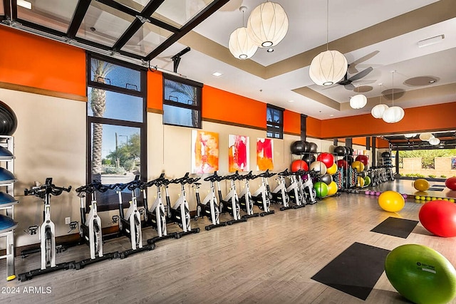 gym with a tray ceiling, wood-type flooring, and ceiling fan