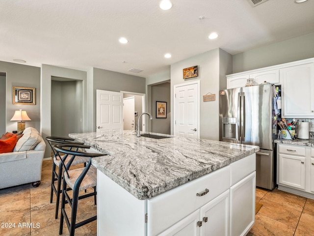 kitchen with an island with sink, stainless steel fridge with ice dispenser, white cabinetry, and sink