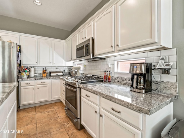 kitchen with light stone counters, stainless steel appliances, backsplash, white cabinetry, and a textured ceiling