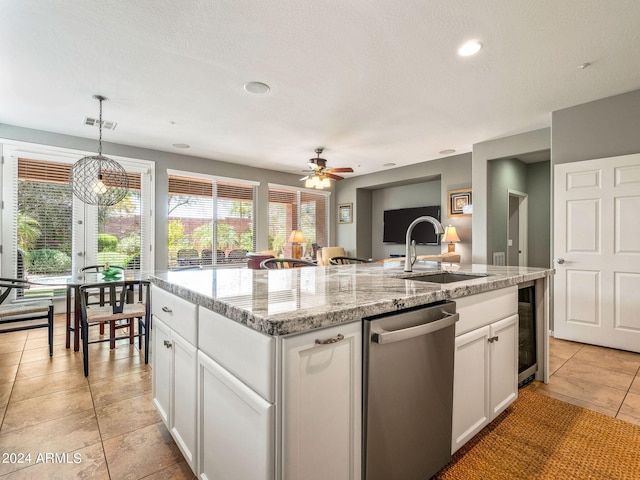 kitchen with light stone counters, decorative light fixtures, white cabinets, stainless steel dishwasher, and a kitchen island with sink