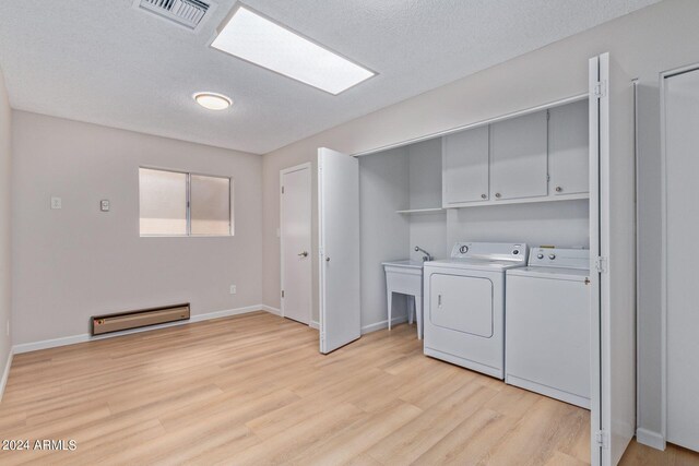 laundry area featuring a baseboard heating unit, light hardwood / wood-style floors, independent washer and dryer, cabinets, and a textured ceiling