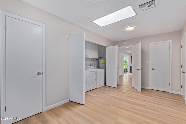 laundry room featuring a skylight, washing machine and dryer, light hardwood / wood-style flooring, cabinets, and a textured ceiling