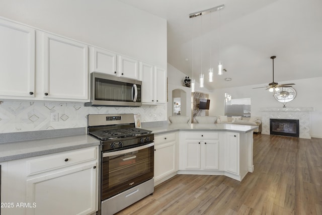 kitchen with a premium fireplace, appliances with stainless steel finishes, white cabinetry, vaulted ceiling, and kitchen peninsula