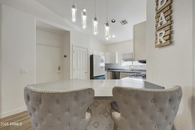 kitchen with lofted ceiling, hanging light fixtures, stainless steel dishwasher, kitchen peninsula, and white fridge