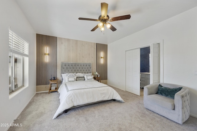 bedroom featuring connected bathroom, wooden walls, light colored carpet, and ceiling fan