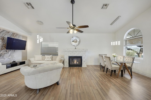 living room featuring vaulted ceiling, ceiling fan, a fireplace, and light hardwood / wood-style floors