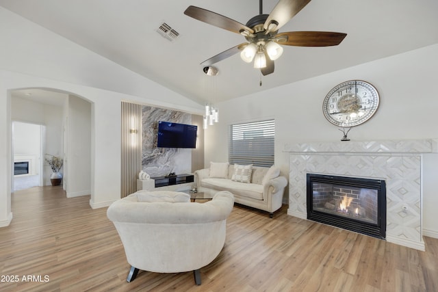 living room featuring light hardwood / wood-style flooring, vaulted ceiling, a tile fireplace, and ceiling fan