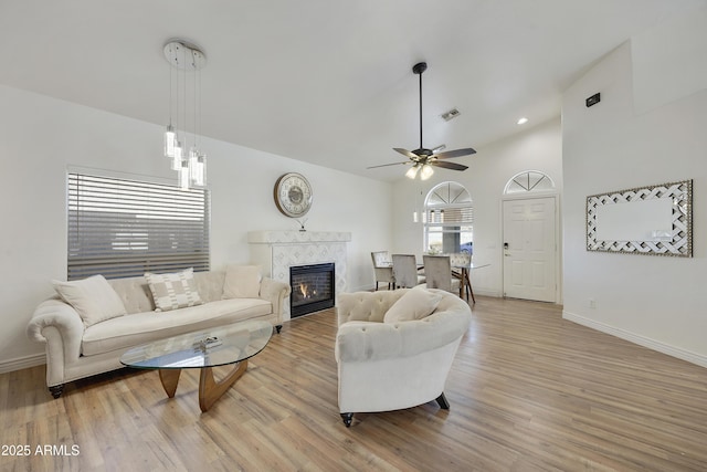 living room featuring ceiling fan, high vaulted ceiling, a fireplace, and light wood-type flooring