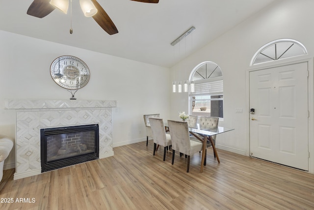 dining space featuring ceiling fan, lofted ceiling, a tile fireplace, and light wood-type flooring