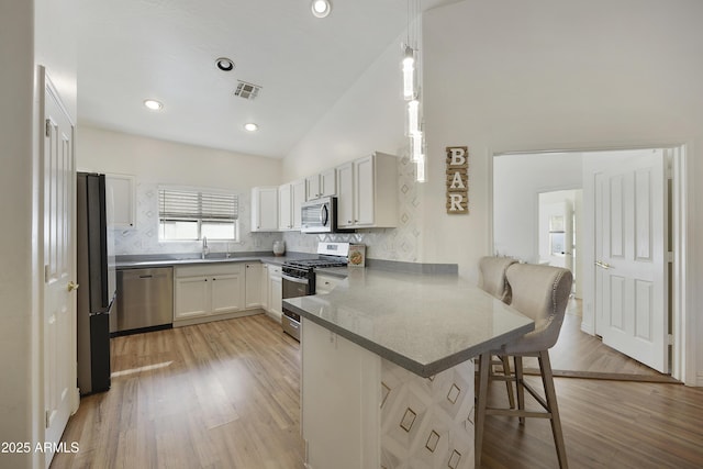 kitchen featuring a breakfast bar area, hanging light fixtures, kitchen peninsula, stainless steel appliances, and white cabinets