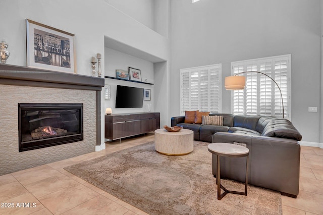 tiled living room featuring a wealth of natural light, a high ceiling, and a stone fireplace