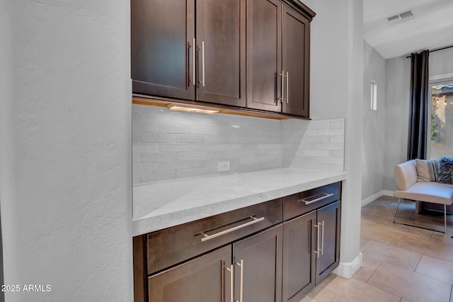 kitchen with dark brown cabinetry, light stone counters, light tile patterned floors, and decorative backsplash