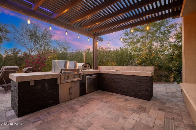 patio terrace at dusk featuring an outdoor kitchen, area for grilling, and a pergola