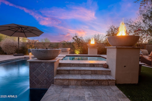 pool at dusk featuring an in ground hot tub and a patio