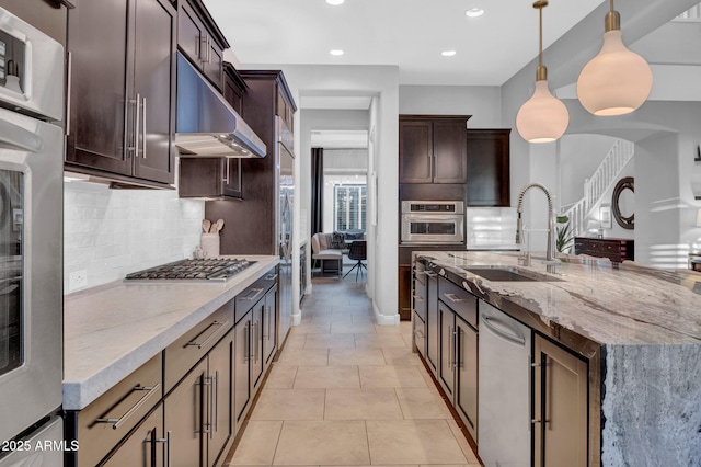 kitchen featuring decorative light fixtures, sink, light stone counters, dark brown cabinetry, and stainless steel gas cooktop