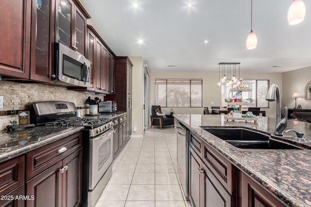 kitchen with sink, hanging light fixtures, light tile patterned floors, appliances with stainless steel finishes, and dark stone counters