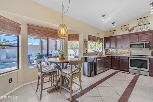 kitchen with a sink, appliances with stainless steel finishes, vaulted ceiling, decorative light fixtures, and backsplash