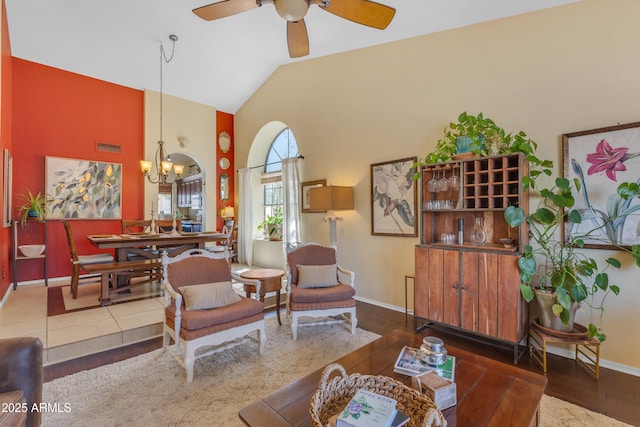 living room with baseboards, high vaulted ceiling, wood finished floors, and ceiling fan with notable chandelier
