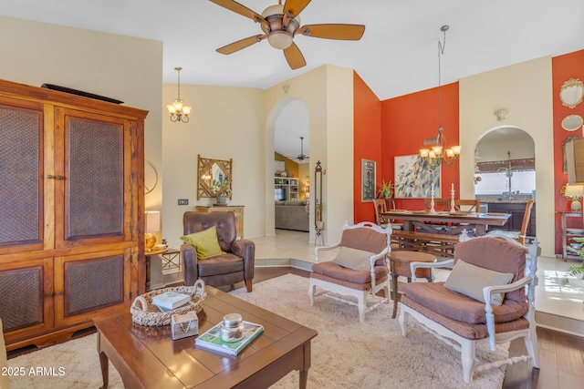 living area featuring high vaulted ceiling, arched walkways, and ceiling fan with notable chandelier