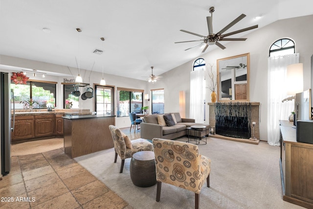 living area with visible vents, a fireplace with raised hearth, a ceiling fan, stone tile flooring, and vaulted ceiling