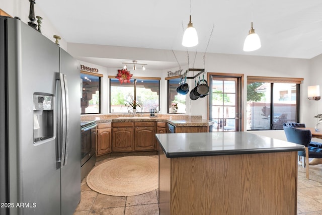 kitchen featuring a sink, stainless steel appliances, dark countertops, decorative light fixtures, and a center island