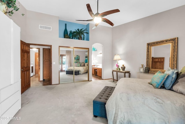 bedroom featuring visible vents, light colored carpet, a closet, a towering ceiling, and arched walkways