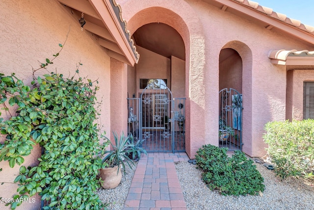 entrance to property with a tile roof, a gate, and stucco siding