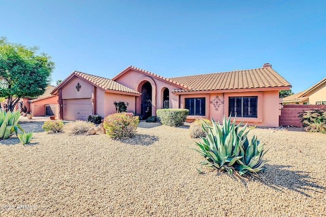 mediterranean / spanish-style house with stucco siding, fence, an attached garage, a chimney, and a tiled roof