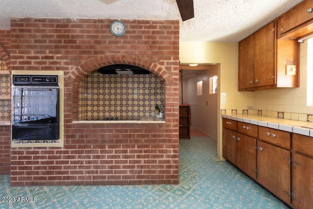 kitchen with brick wall, a textured ceiling, tile countertops, and black appliances