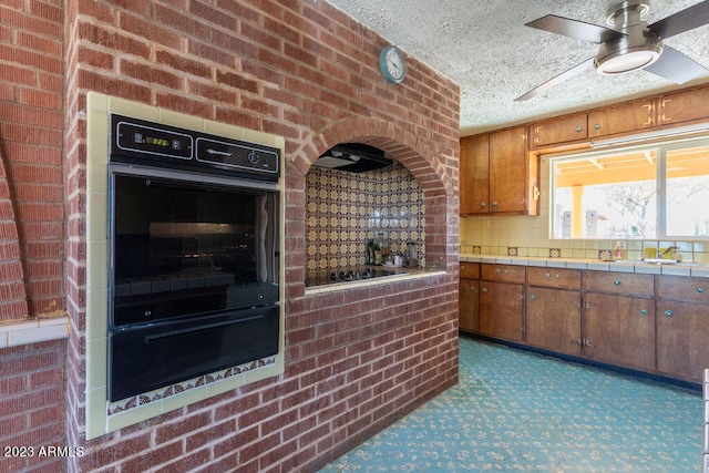 kitchen with brick wall, ceiling fan, a textured ceiling, black appliances, and dark colored carpet