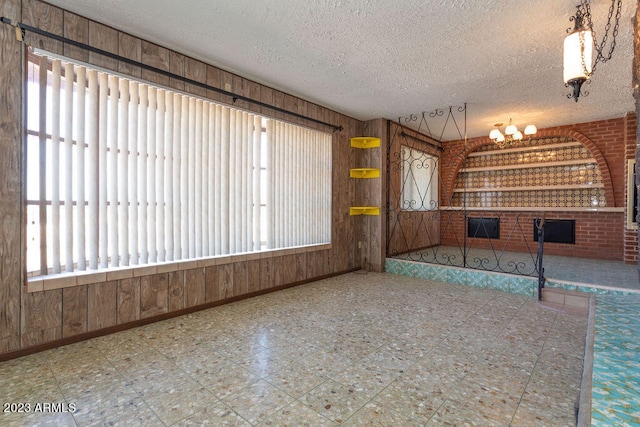 tiled empty room with brick wall, a textured ceiling, wooden walls, and a healthy amount of sunlight