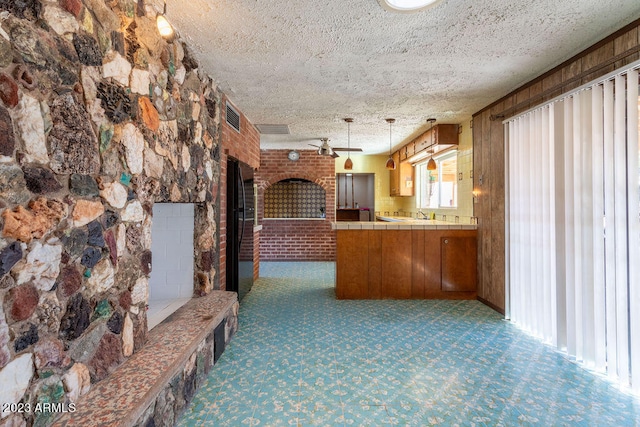 kitchen featuring kitchen peninsula, dark carpet, decorative light fixtures, a textured ceiling, and black fridge