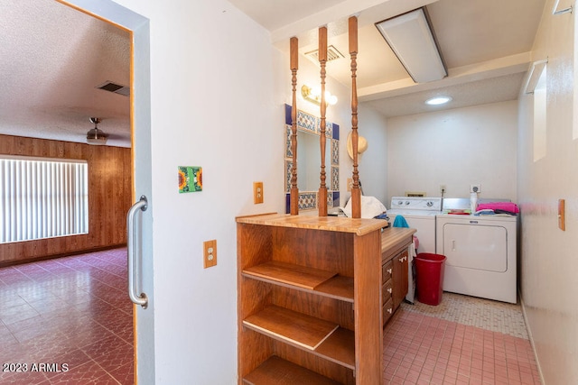 clothes washing area with washer hookup, a textured ceiling, wooden walls, washer and dryer, and dark tile floors