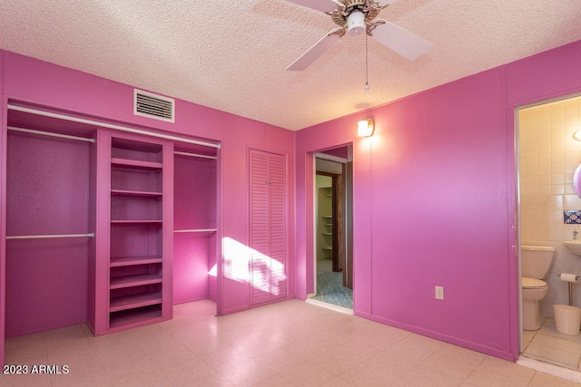 unfurnished bedroom featuring light tile flooring, connected bathroom, ceiling fan, and a textured ceiling