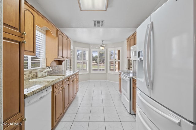 8431 W Utopia Rd, Peoria, AZ 85382 - kitchen with white appliances, light stone counters, backsplash, a ceiling fan, and brown cabinetry