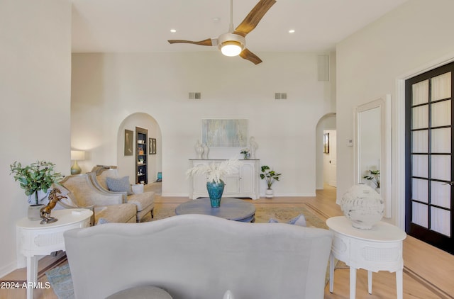 living room with ceiling fan, a towering ceiling, and light wood-type flooring