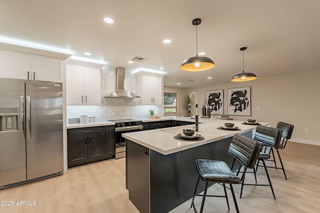 kitchen featuring visible vents, white cabinets, stainless steel appliances, wall chimney range hood, and a kitchen bar