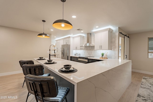 kitchen featuring a barn door, white cabinetry, stainless steel refrigerator with ice dispenser, decorative backsplash, and wall chimney exhaust hood