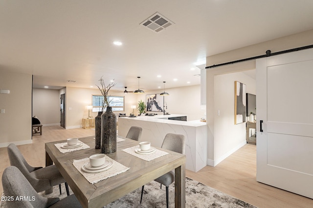 dining space with a barn door, visible vents, baseboards, light wood-type flooring, and recessed lighting