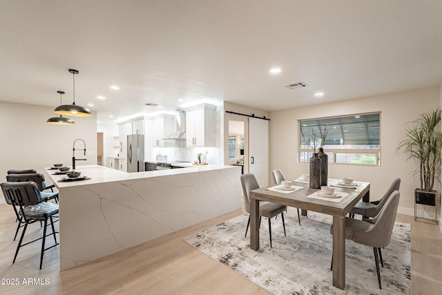 dining space with a barn door, recessed lighting, visible vents, and light wood-style floors