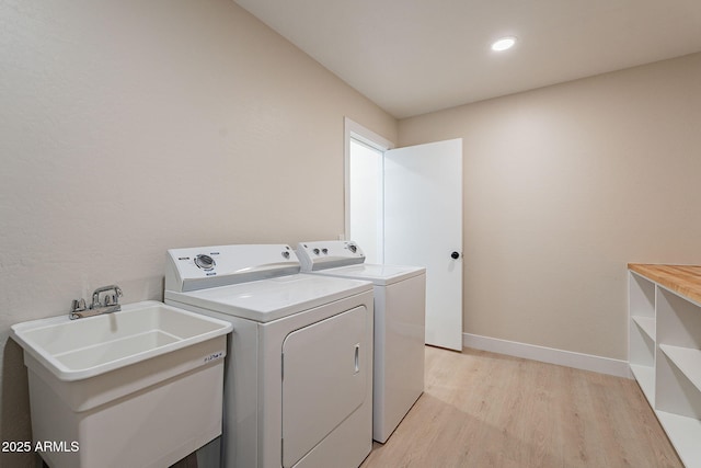 laundry area with laundry area, a sink, baseboards, light wood-style floors, and independent washer and dryer