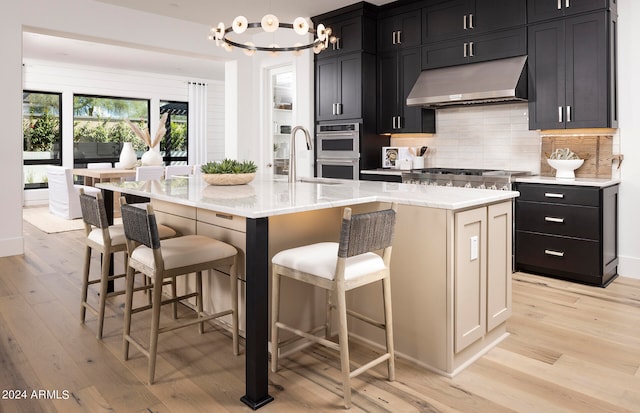 kitchen with a kitchen bar, light hardwood / wood-style floors, a kitchen island with sink, and a notable chandelier