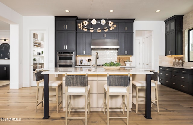 kitchen featuring a notable chandelier, a breakfast bar, light hardwood / wood-style floors, an island with sink, and tasteful backsplash