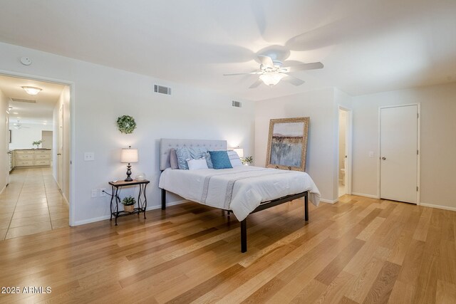 bedroom with light wood finished floors, ensuite bath, visible vents, and baseboards