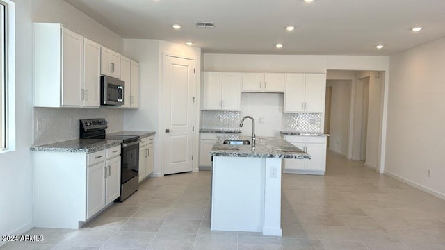 kitchen with white cabinets, appliances with stainless steel finishes, stone countertops, and a kitchen island with sink