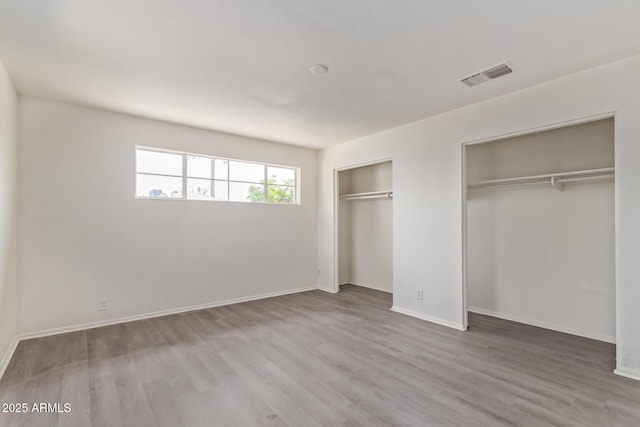 unfurnished bedroom with wood finished floors, baseboards, multiple closets, and visible vents