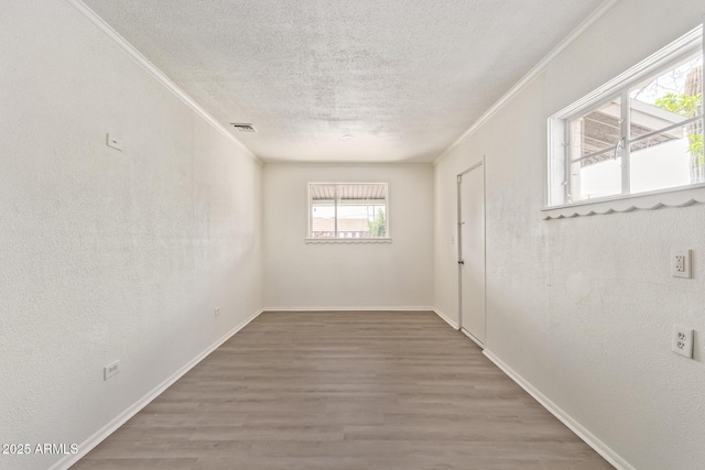 empty room featuring wood finished floors, ornamental molding, a textured ceiling, and visible vents