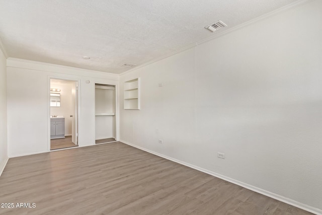 unfurnished bedroom with crown molding, a textured ceiling, visible vents, a closet, and wood finished floors